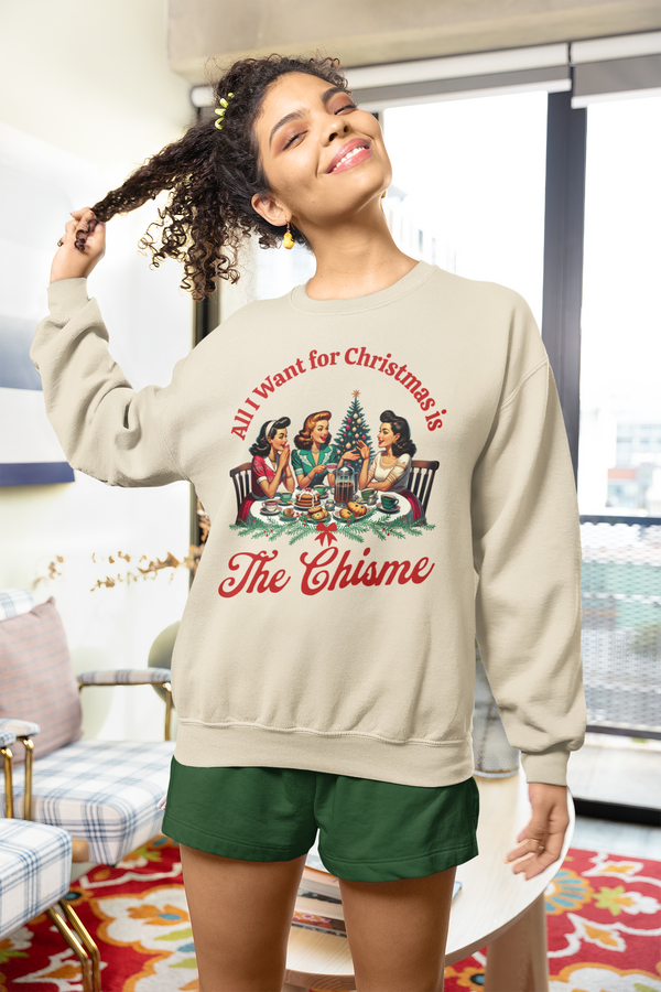 Woman wearing a beige sweatshirt with a graphic design and text, standing in a room with a couch and window in the background.