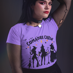 Person wearing a purple t-shirt with 'Comadre Crew' design against a dark background