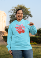 Person wearing a hoodie with a pink bow and red cherries graphic featuring the text 'Chinga La Migra' in a stylized font