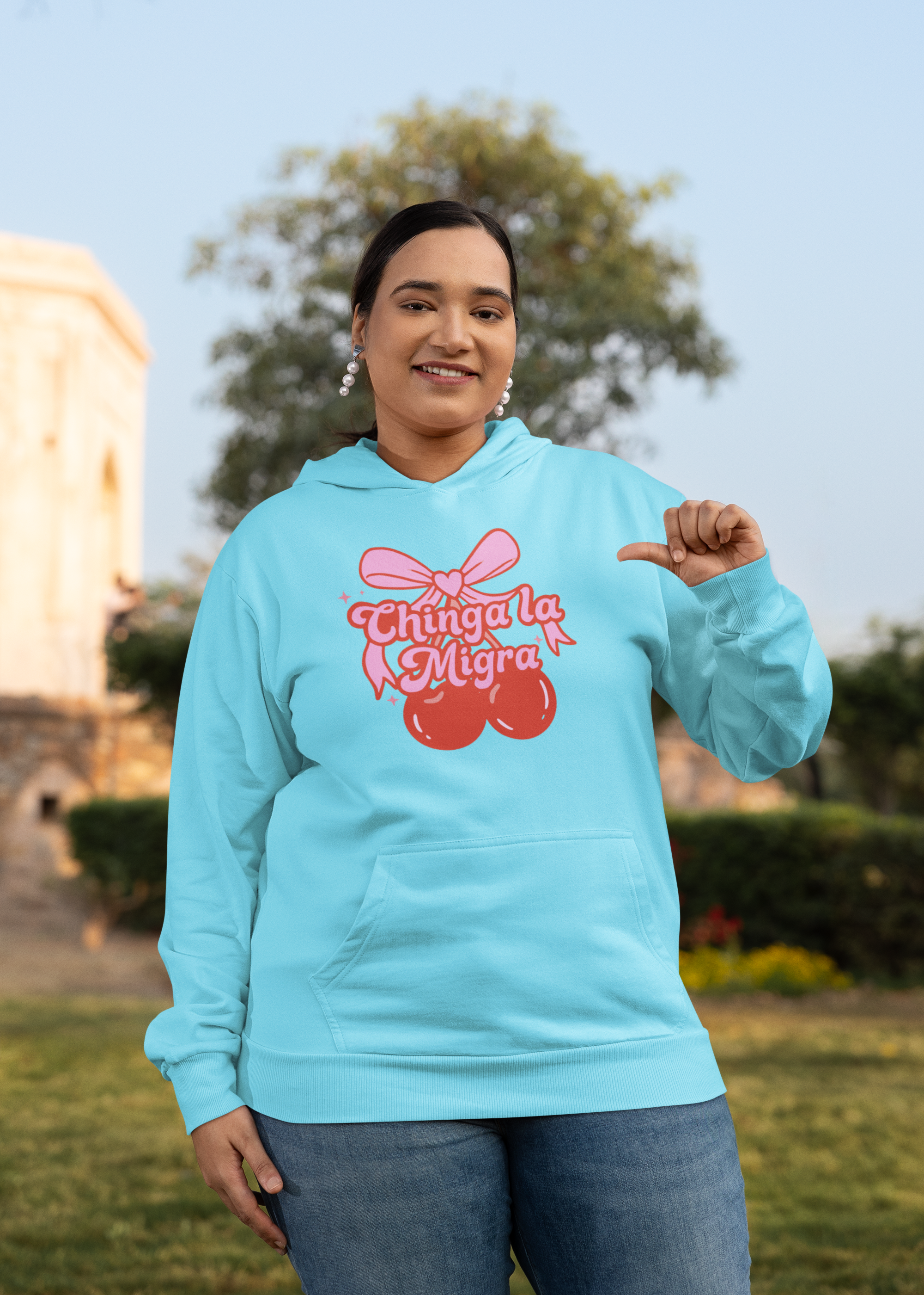 Person wearing a hoodie with a pink bow and red cherries graphic featuring the text 'Chinga La Migra' in a stylized font