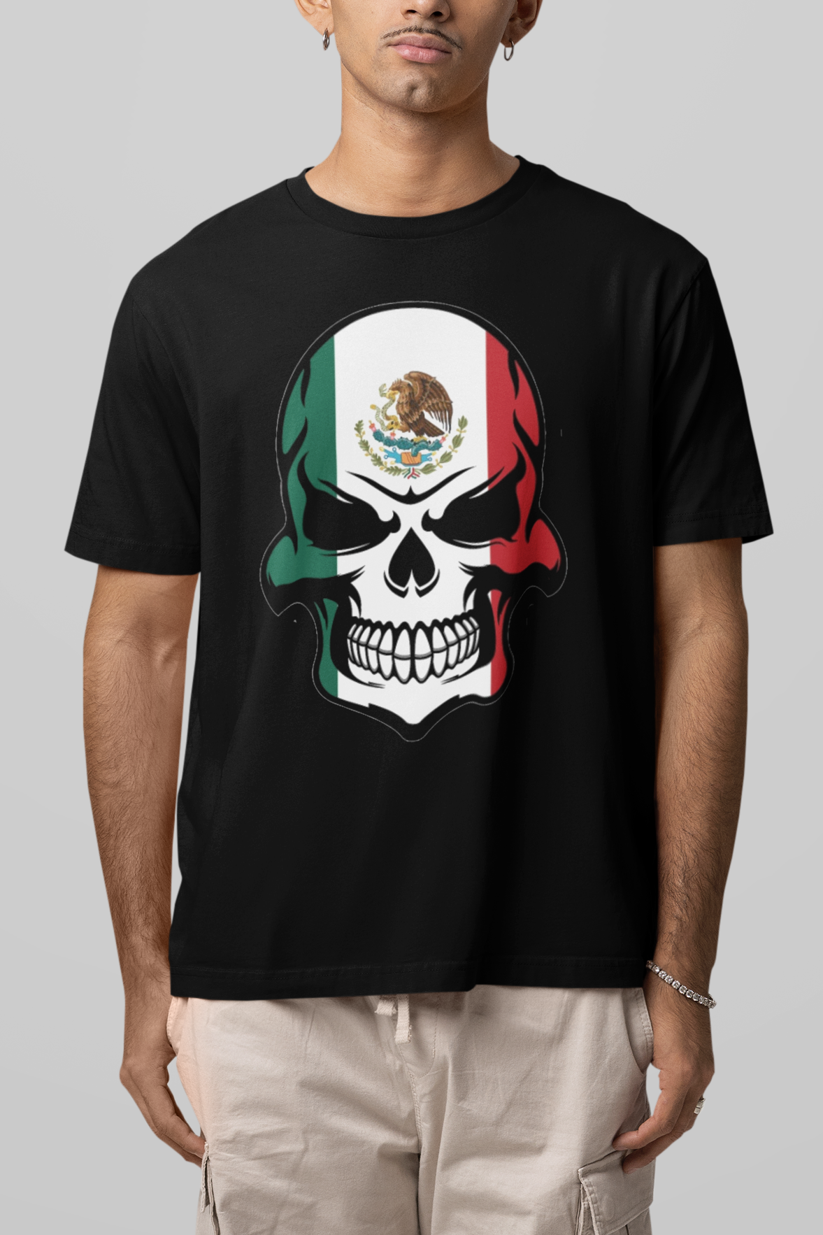 Person wearing a black t-shirt with a skull design featuring the Mexican flag on a gray background