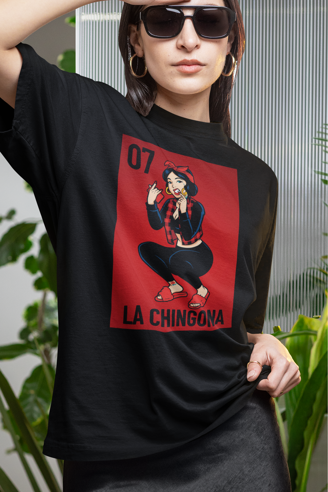 Woman wearing a black t-shirt with a graphic design in an outdoor setting with plants.