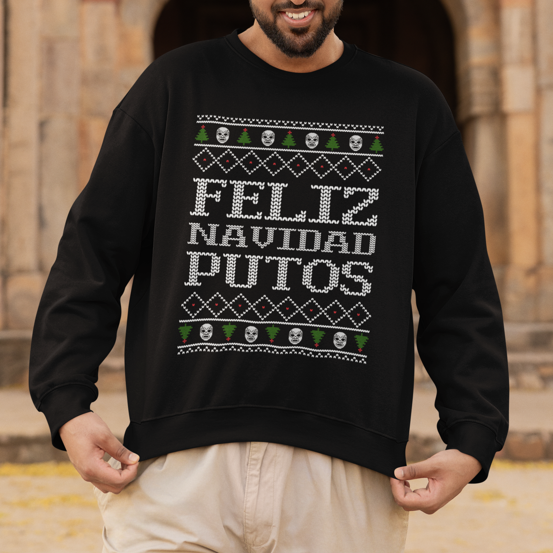 Man wearing a black sweater with 'Feliz Navidad Putos' text in front of an architectural background