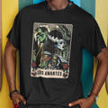 Person wearing a black t-shirt with 'Los Amantes' design and a cap, standing against a colorful wall.