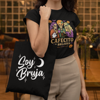 Woman wearing a black t-shirt with a graphic design and holding a black tote bag with 'Soy Bruja' text.